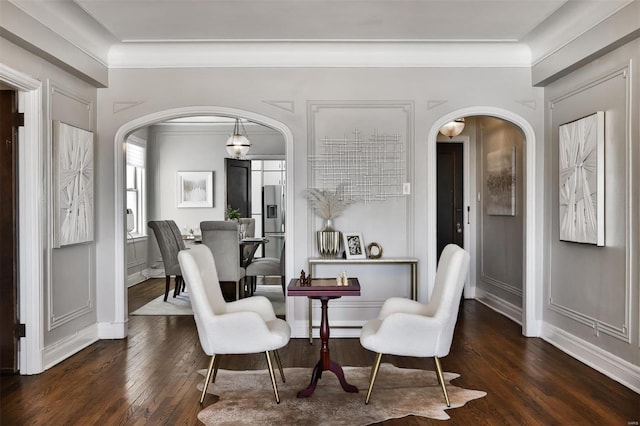 living area featuring arched walkways, hardwood / wood-style floors, crown molding, and baseboards