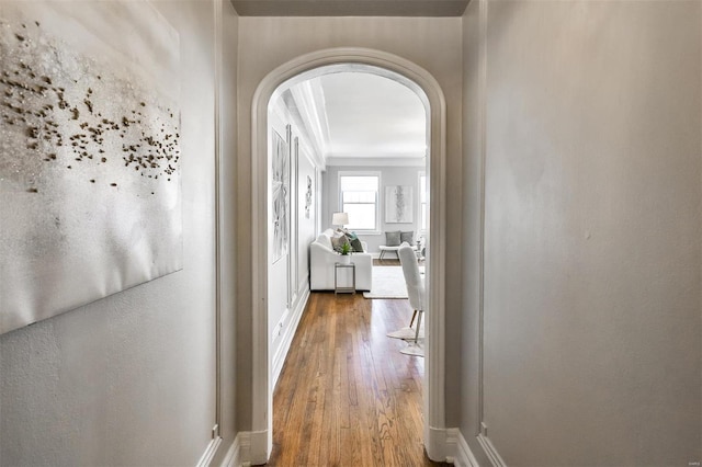 hall featuring baseboards, arched walkways, and wood finished floors