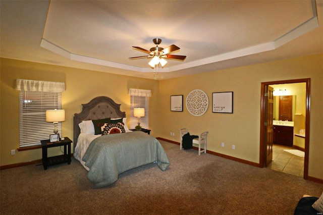 carpeted bedroom with ceiling fan, connected bathroom, and a tray ceiling