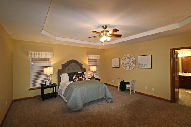 carpeted bedroom with ceiling fan, connected bathroom, and a raised ceiling