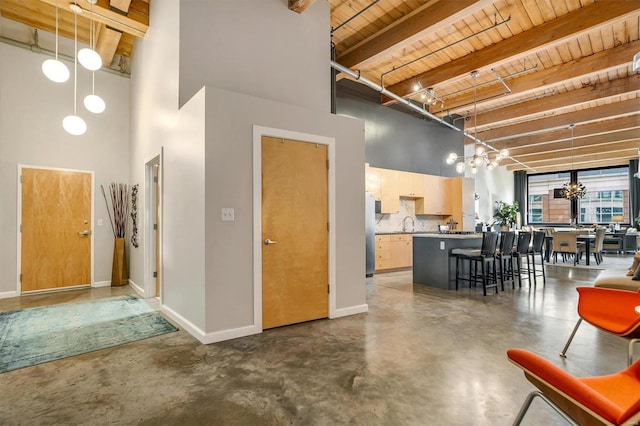 interior space with pendant lighting, wood ceiling, light brown cabinetry, beam ceiling, and a breakfast bar area