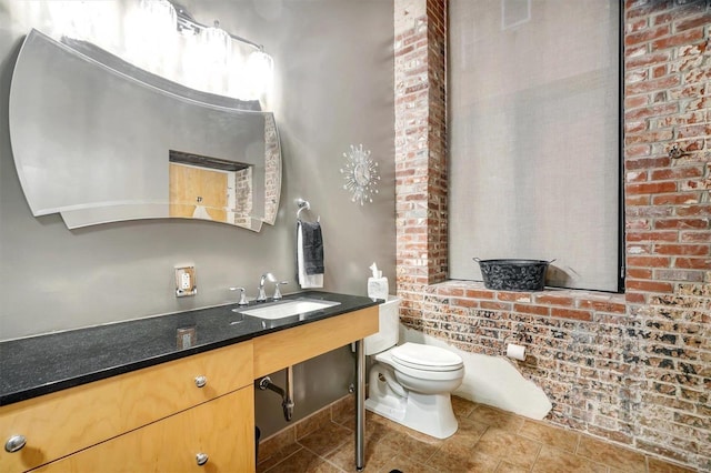 bathroom featuring brick wall, toilet, and vanity