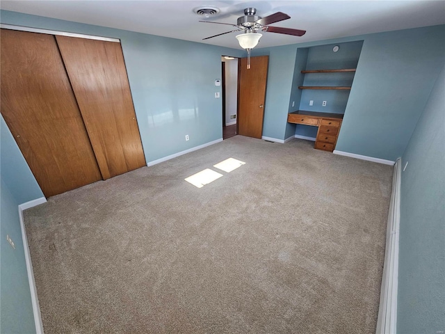 unfurnished bedroom featuring built in desk, a closet, ceiling fan, and carpet flooring