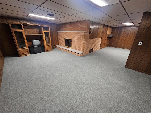 basement featuring a paneled ceiling, a fireplace, wood walls, and light colored carpet