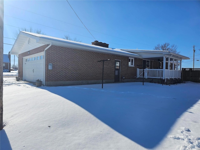 snow covered rear of property with covered porch and a garage