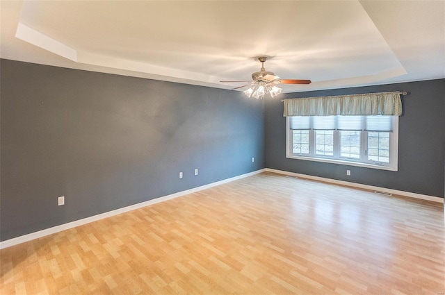 unfurnished room featuring a tray ceiling, ceiling fan, and light wood-type flooring