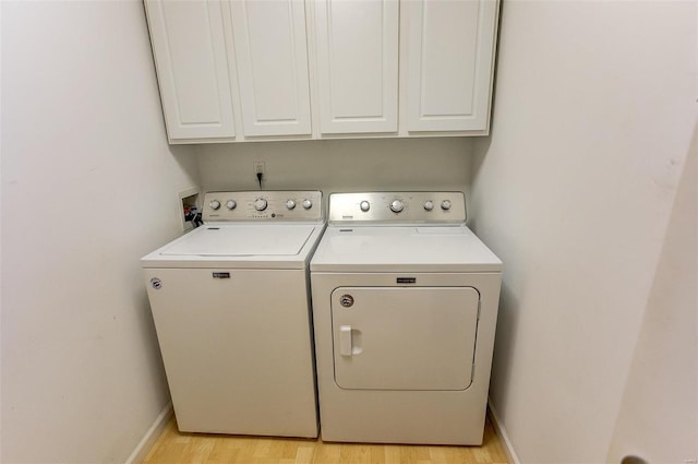 washroom featuring cabinets, washing machine and clothes dryer, and light hardwood / wood-style flooring