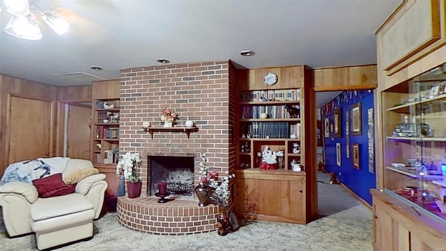 carpeted living room with built in shelves, wood walls, and a brick fireplace