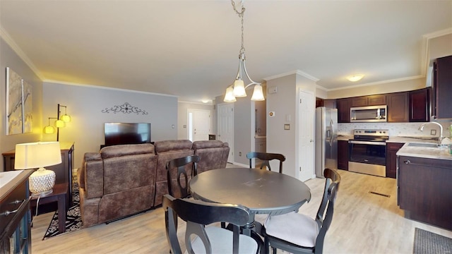 dining space with light wood-type flooring, ornamental molding, sink, and a notable chandelier