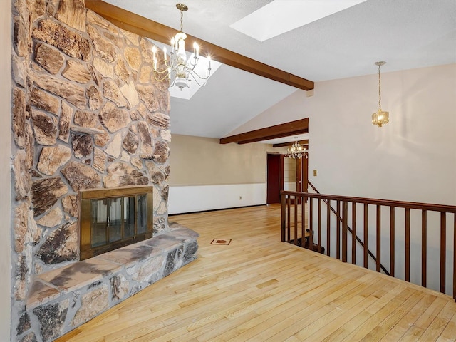 living room with an inviting chandelier, a stone fireplace, lofted ceiling with skylight, and hardwood / wood-style flooring