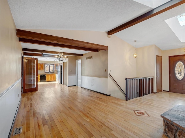 unfurnished living room featuring an inviting chandelier, vaulted ceiling with skylight, a textured ceiling, and light wood-type flooring