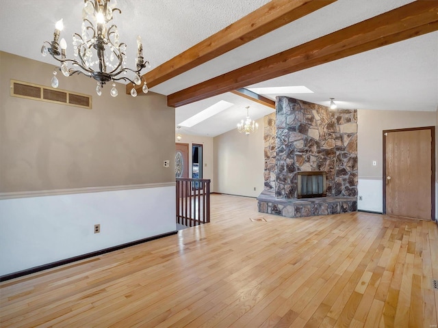 unfurnished living room featuring lofted ceiling with skylight, an inviting chandelier, a fireplace, a textured ceiling, and light wood-type flooring