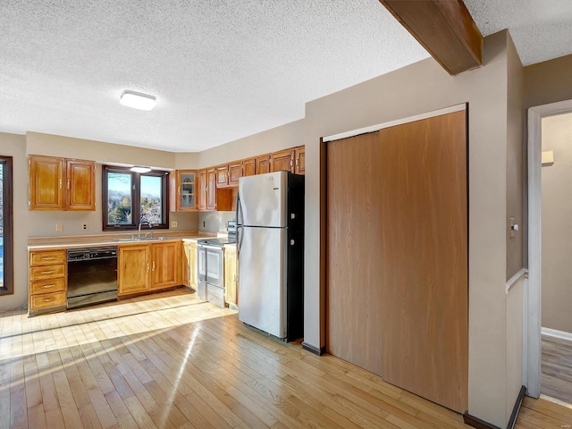 kitchen with sink, a textured ceiling, light wood-type flooring, appliances with stainless steel finishes, and beam ceiling