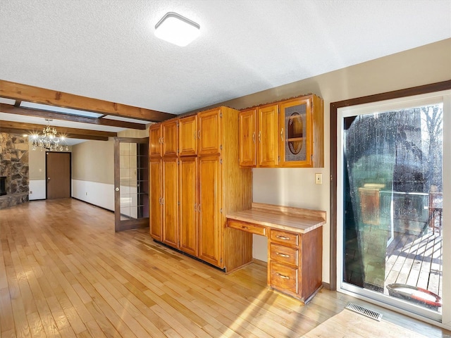 kitchen with beam ceiling, a fireplace, built in desk, light hardwood / wood-style floors, and a textured ceiling