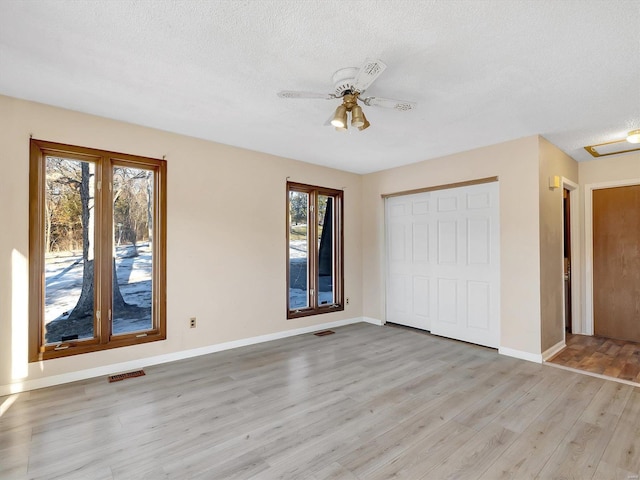 unfurnished bedroom with multiple windows, a textured ceiling, light hardwood / wood-style floors, and a closet