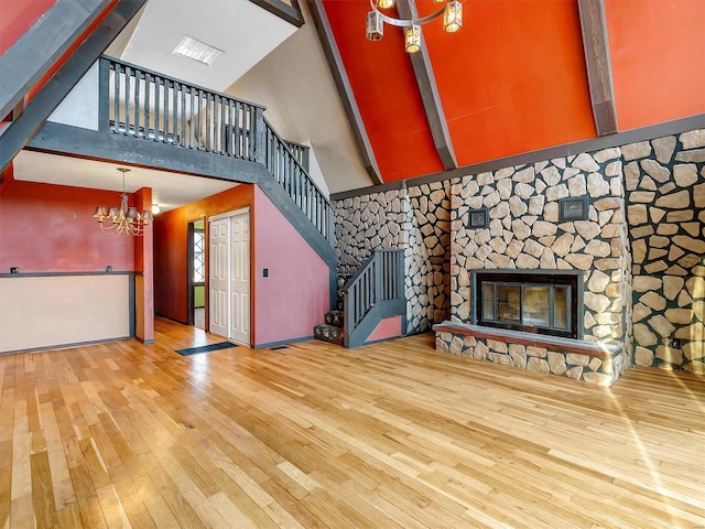 unfurnished living room with a towering ceiling, a stone fireplace, hardwood / wood-style floors, and a notable chandelier