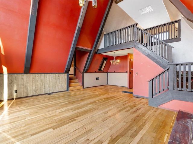 unfurnished living room featuring an inviting chandelier, high vaulted ceiling, and light hardwood / wood-style floors