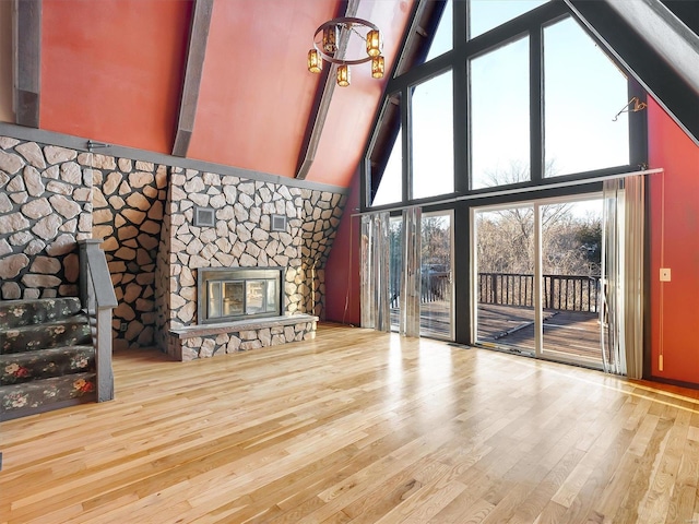 unfurnished living room with beamed ceiling, a stone fireplace, high vaulted ceiling, and light wood-type flooring