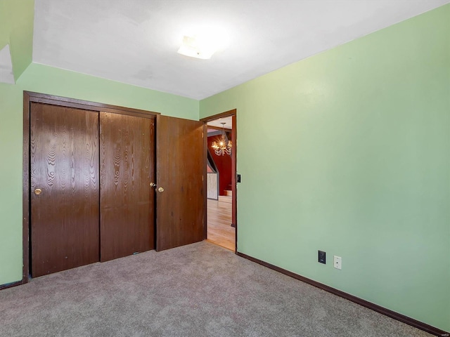 unfurnished bedroom featuring an inviting chandelier, light colored carpet, and a closet