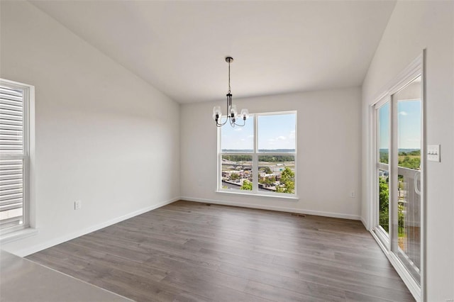 unfurnished dining area featuring vaulted ceiling, hardwood / wood-style flooring, a notable chandelier, and plenty of natural light