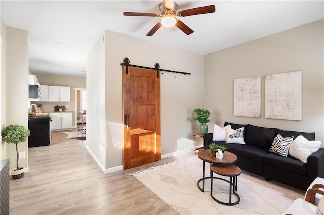 living room featuring sink, ceiling fan, a barn door, and light hardwood / wood-style flooring