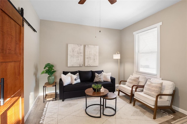 living room with light wood-type flooring, ceiling fan, and a barn door