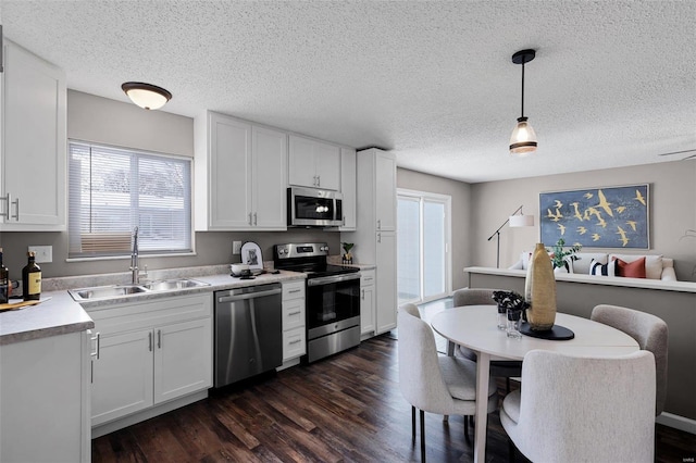 kitchen featuring appliances with stainless steel finishes, decorative light fixtures, white cabinetry, a healthy amount of sunlight, and sink