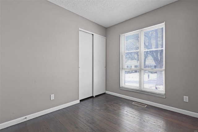 unfurnished bedroom featuring a closet, dark hardwood / wood-style floors, multiple windows, and a textured ceiling