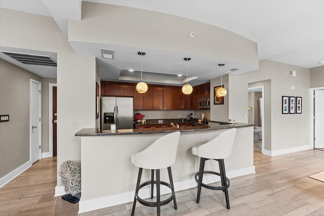 kitchen featuring appliances with stainless steel finishes, hanging light fixtures, a raised ceiling, kitchen peninsula, and light wood-type flooring