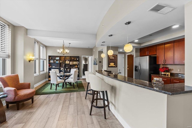 kitchen featuring stainless steel refrigerator with ice dispenser, dark stone countertops, hanging light fixtures, and light wood-type flooring