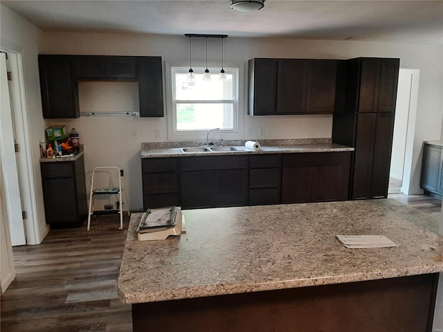 kitchen featuring pendant lighting, light stone counters, hardwood / wood-style flooring, sink, and dark brown cabinets