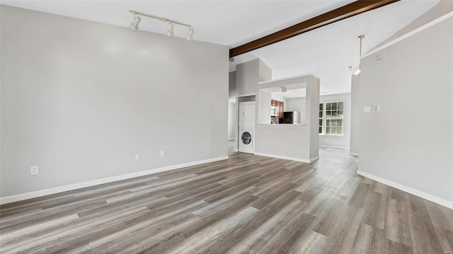 unfurnished living room featuring hardwood / wood-style flooring, track lighting, and vaulted ceiling with beams