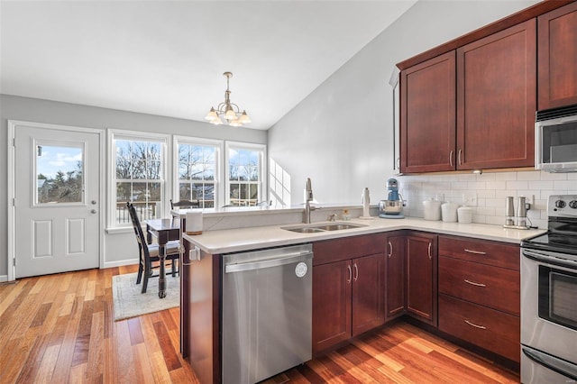 kitchen with kitchen peninsula, vaulted ceiling, a notable chandelier, appliances with stainless steel finishes, and sink