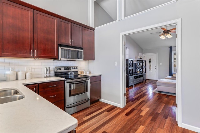 kitchen with appliances with stainless steel finishes, dark hardwood / wood-style flooring, backsplash, and ceiling fan