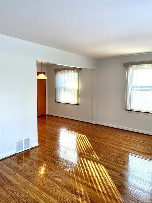 empty room with a wealth of natural light and dark hardwood / wood-style flooring