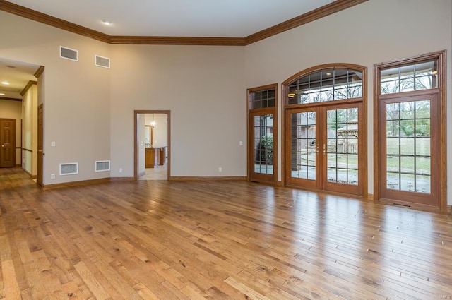 unfurnished living room with a high ceiling, french doors, crown molding, and light hardwood / wood-style floors