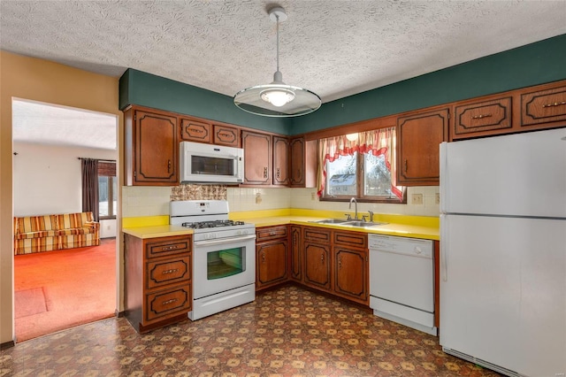 kitchen featuring white appliances, dark floors, brown cabinets, light countertops, and a sink