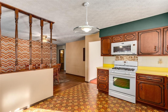 kitchen featuring a textured ceiling, dark floors, white appliances, light countertops, and tasteful backsplash