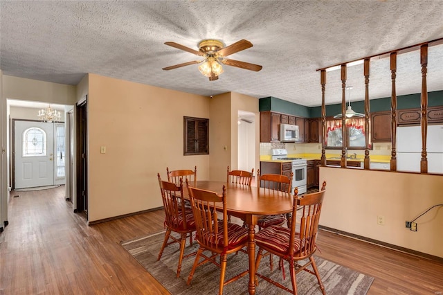 dining area featuring a textured ceiling, baseboards, wood finished floors, and ceiling fan with notable chandelier