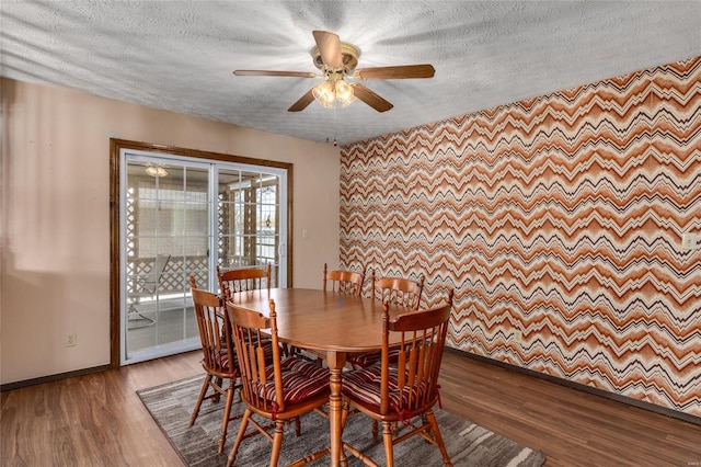 dining room with an accent wall, a textured ceiling, baseboards, and wood finished floors