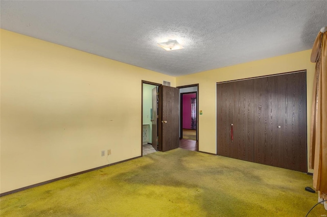 unfurnished bedroom featuring a textured ceiling, carpet floors, visible vents, baseboards, and a closet