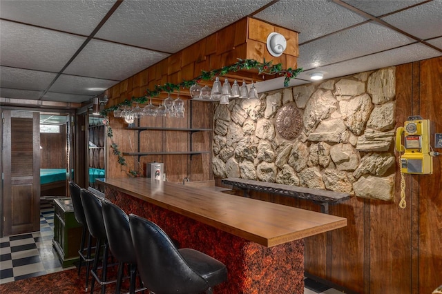 bar with a paneled ceiling, wooden walls, a dry bar, and tile patterned floors