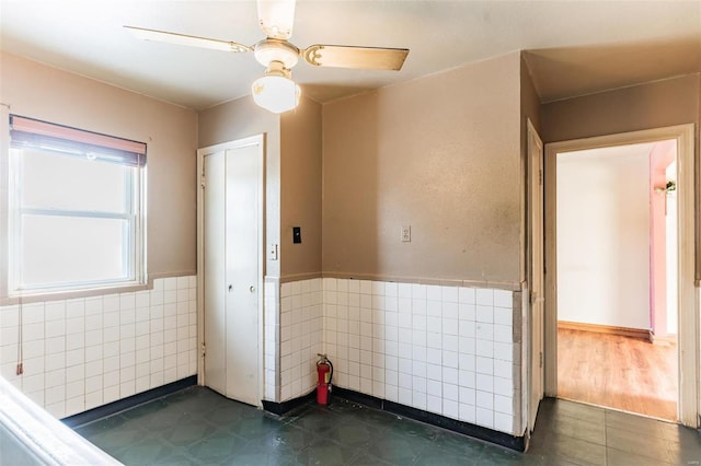 interior space with ceiling fan and tile walls