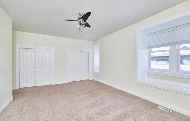 unfurnished bedroom featuring ceiling fan, multiple closets, and carpet floors