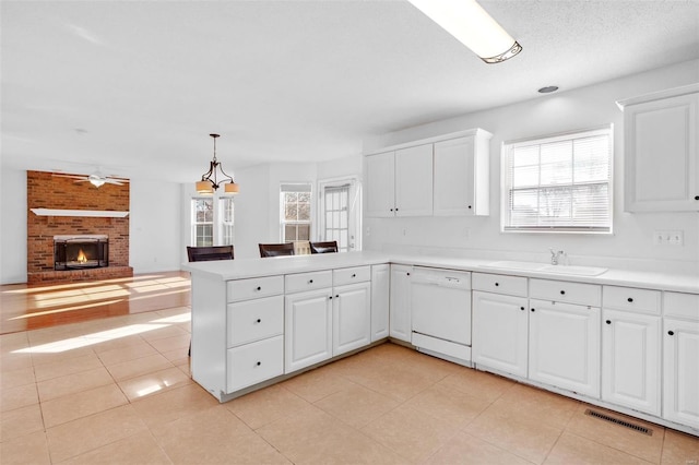 kitchen with kitchen peninsula, a brick fireplace, sink, and white dishwasher