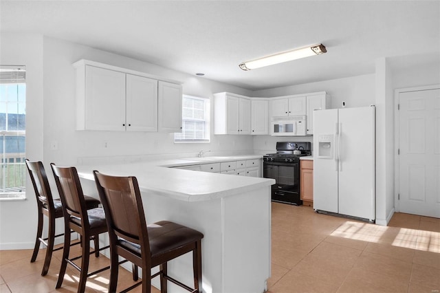 kitchen featuring light tile patterned floors, kitchen peninsula, white appliances, a kitchen breakfast bar, and white cabinets