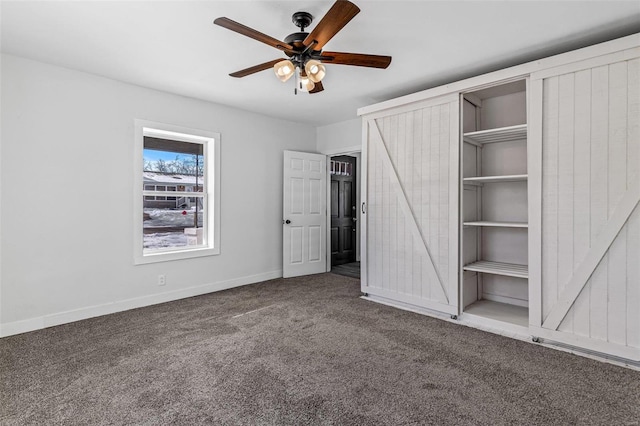 unfurnished bedroom featuring ceiling fan, a barn door, and carpet floors