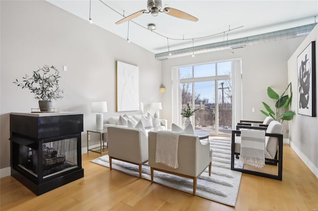 living room with ceiling fan, baseboards, and wood finished floors