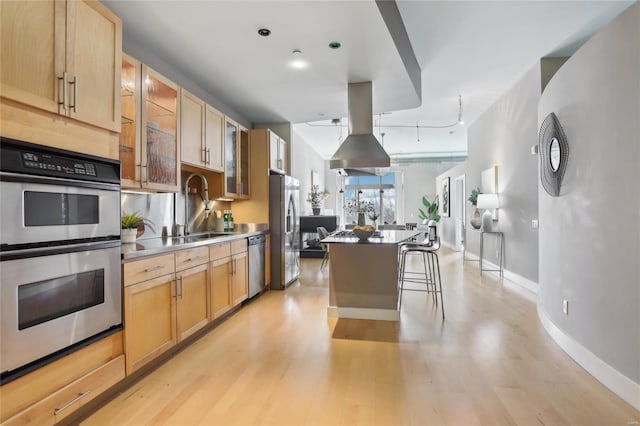 kitchen with appliances with stainless steel finishes, glass insert cabinets, a center island, light wood-type flooring, and a sink