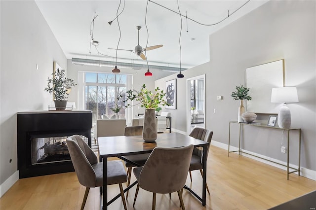 dining space featuring light wood finished floors, a multi sided fireplace, and baseboards